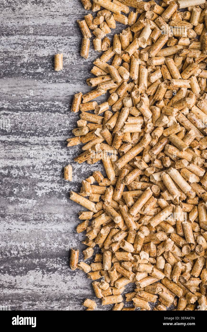 Piccoli pellet di legno dorato sparsi su una superficie di cemento testurizzato, che rappresentano il combustibile a biomassa, il riscaldamento rinnovabile, il combustibile per stufe e l'energia sostenibile per il riscaldamento domestico, il giardinaggio e l'uso di lettiere per animali. Foto Stock
