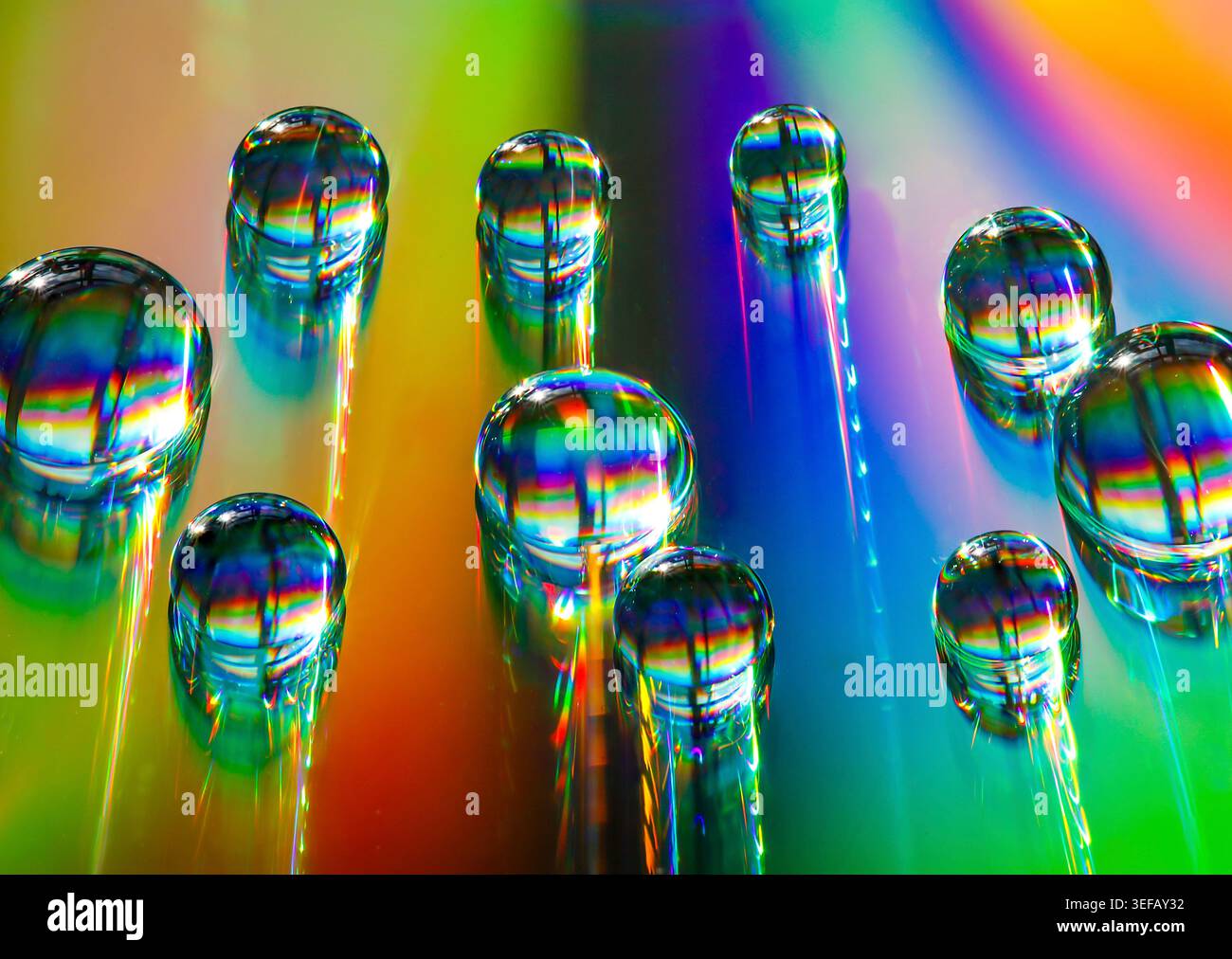 Le gocce d'acqua iridescenti scorrono attraverso lo spettro dell'arcobaleno, creando una vibrante danza astratta di luce, movimento e riflesso. Foto Stock
