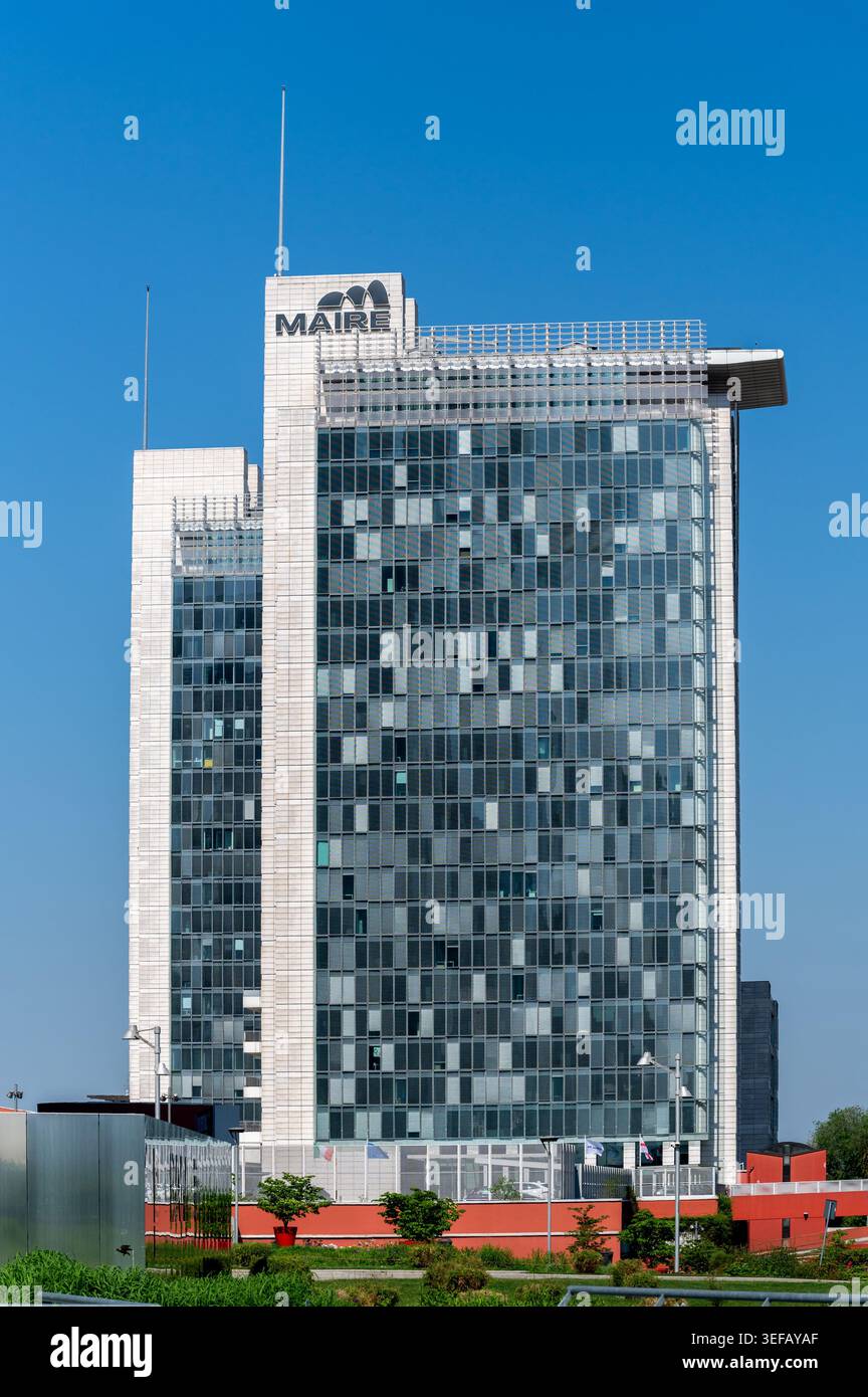 Milano, Lombardia, Italia - 22 aprile 2026: Moderno edificio della sede di MAIRE con facciata in vetro e logo su un cielo azzurro Foto Stock