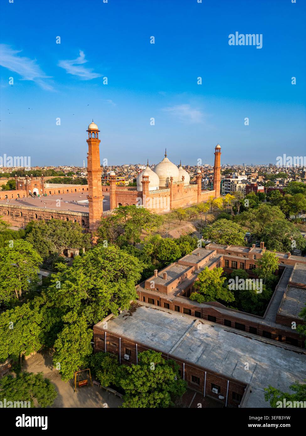 Vista della Moschea Badshahi a Lahore che mostra la grande struttura circondata dal verde e dalla vita cittadina nel Punjab durante il giorno Foto Stock
