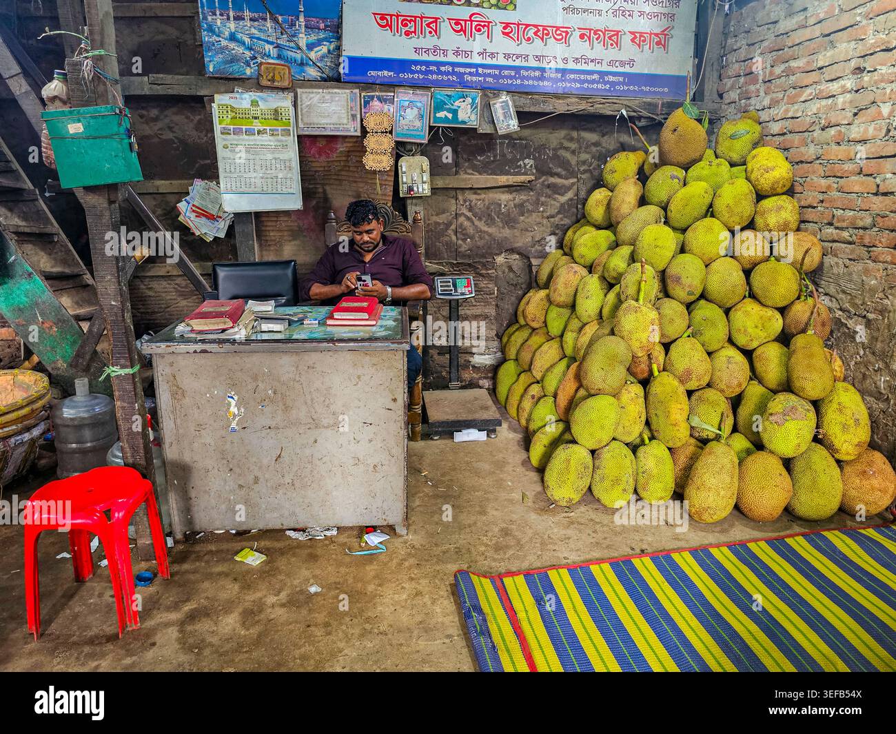 Giacchino gigante impilato in un negozio con un lavoratore che usa un telefono cellulare in un mercato del pesce in Bangladesh Foto Stock