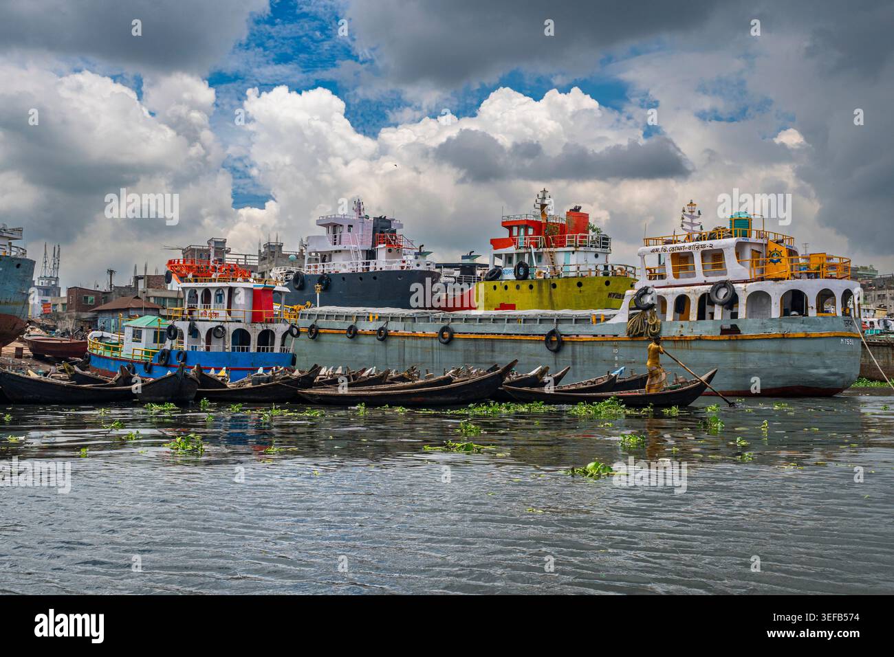 Le barche da pesca navigano lungo il fiume Buriganga mentre le navi più grandi riposano lungo la riva di Dacca, Bangladesh Foto Stock