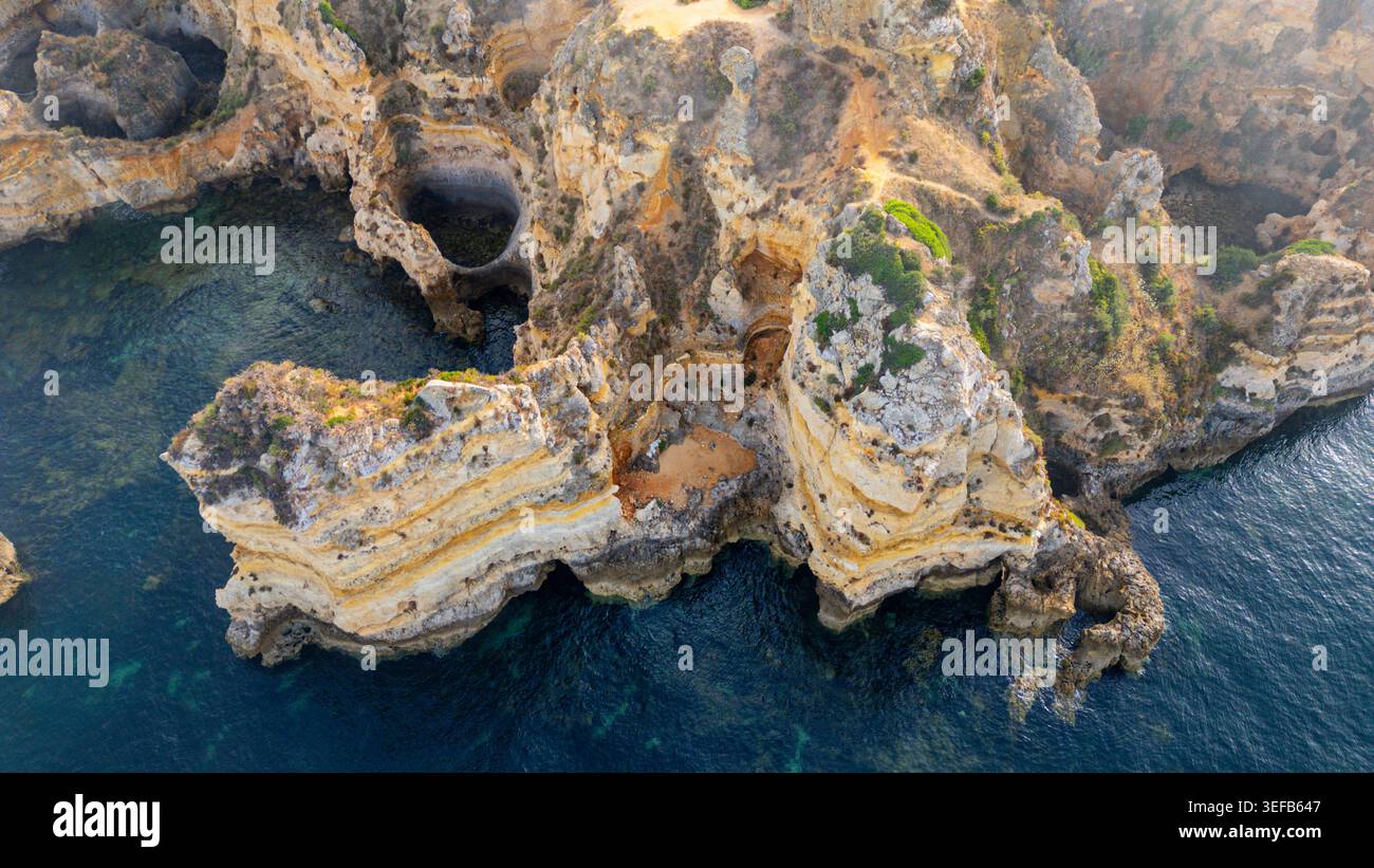 Tramonto sulle scogliere che mostrano onde e rocce lungo la costa dell'Algarve in Portogallo Foto Stock