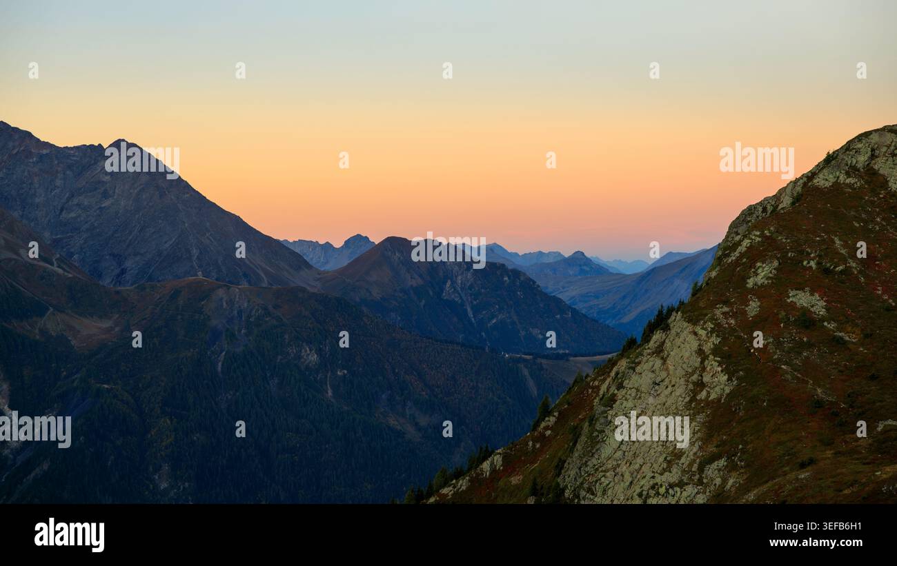 Rifugio de Bellachat, Francia - 20.09.2025: Una vasta e panoramica vista di aspre cime di montagna e profonde valli sotto un vivace crepuscolo arancione e ciano sk Foto Stock