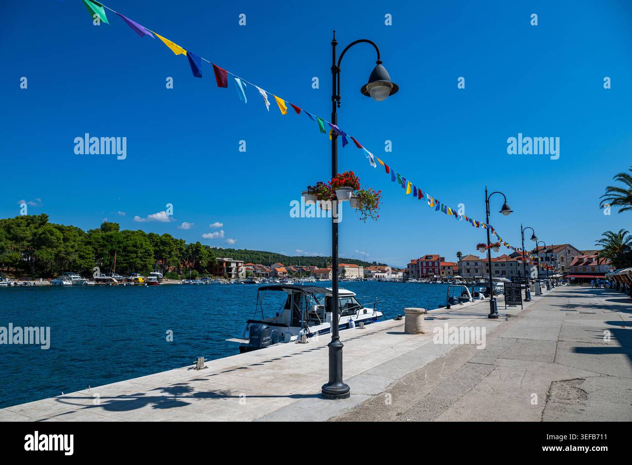 Bandiere colorate decorano il lungomare vicino alle barche a Stari Grad, mentre alberi ed edifici fiancheggiano la baia in Croazia Foto Stock