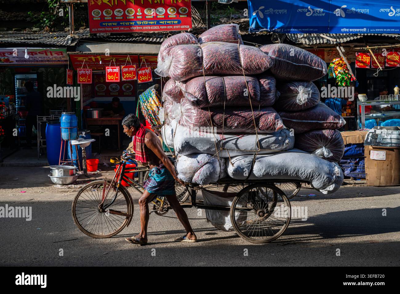 Il trasporto di merci su un risciò attraverso le strade trafficate di Dacca, Bangladesh, durante il giorno è una cosa comune Foto Stock