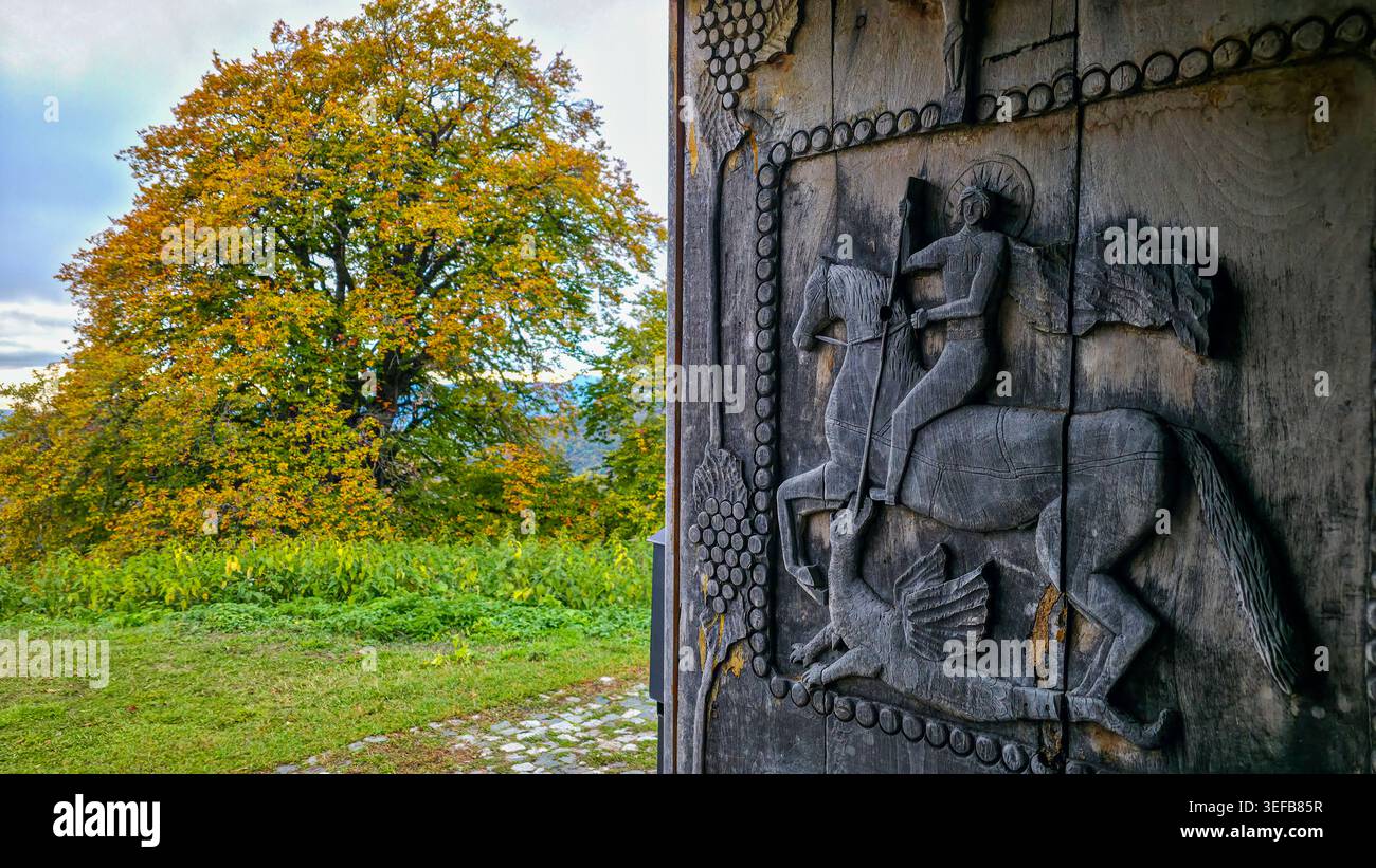 Porta intagliata in legno con cavaliere nella chiesa di San Giorgio nell'Ossezia del Sud, Russia, circondata dalla natura e dai cambiamenti stagionali Foto Stock