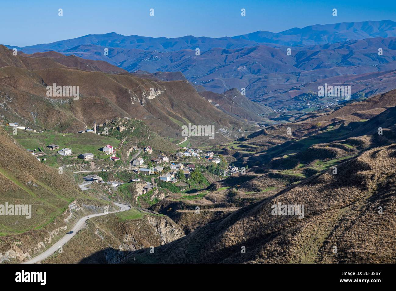 Vista della valle di montagna che mostra i pendii collinari e i piccoli villaggi nel Daghestan, Russia, con una strada tortuosa in primo piano Foto Stock
