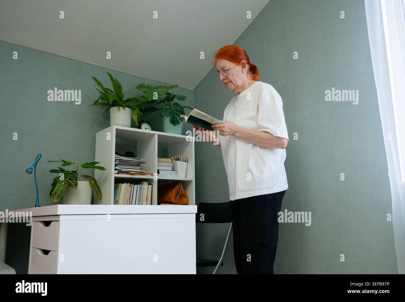 Una donna anziana è completamente affascinata da un libro emozionante mentre si trova nel suo spazio abitativo. hobby mostra come la lettura può essere un'attività emozionante e mentalmente coinvolgente per gli adulti più anziani. Foto Stock