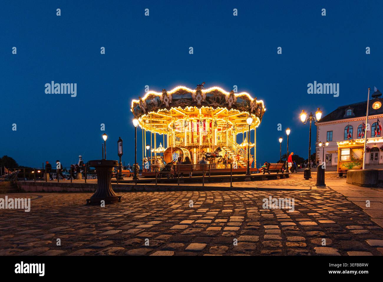 La giostra d'epoca illumina il lungomare del porto di notte, attirando visitatori a Honfleur, Normandia, Francia Foto Stock