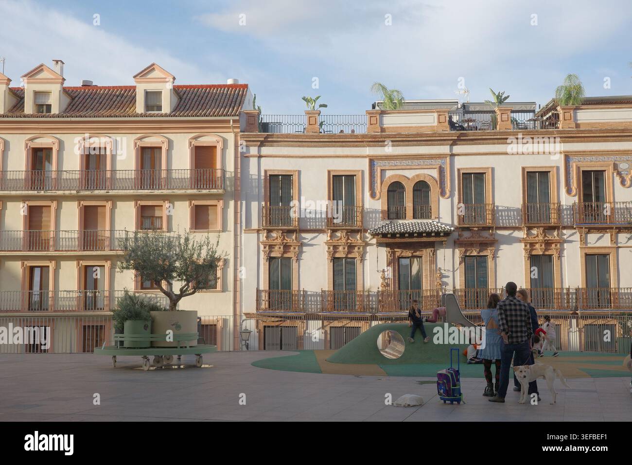 Famiglie con bambini e cani in un parco giochi moderno circondato da facciate ornamentali di edifici storici in Plaza de la Encarnacion, Siviglia, Andalusia Foto Stock