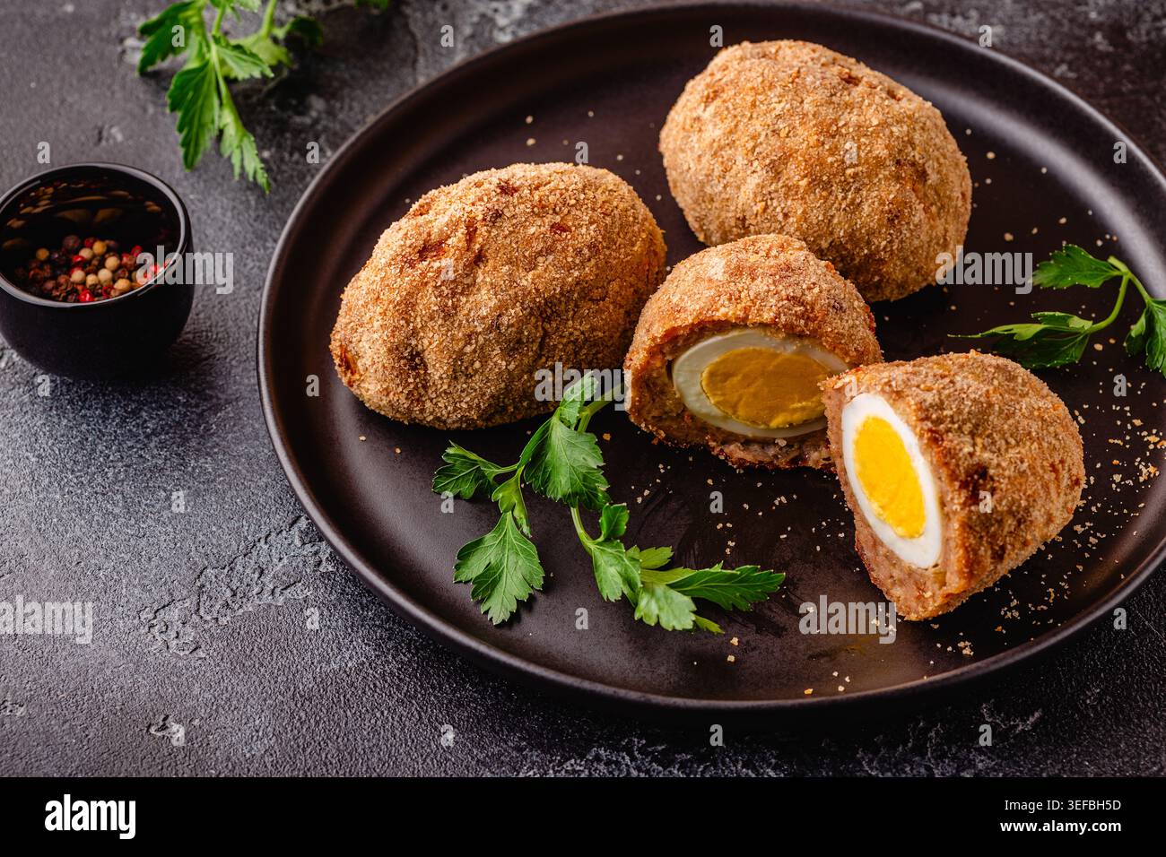 Uova tradizionali di Scotch su un piatto nero, su sfondo scuro. Foto Stock