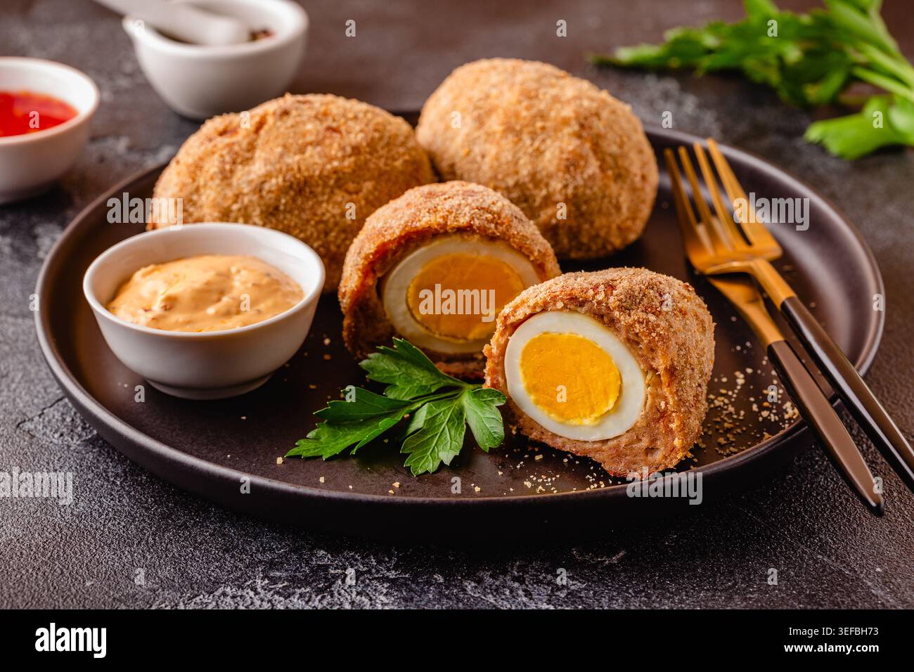Uova tradizionali di Scotch su un piatto nero, su sfondo scuro. Foto Stock