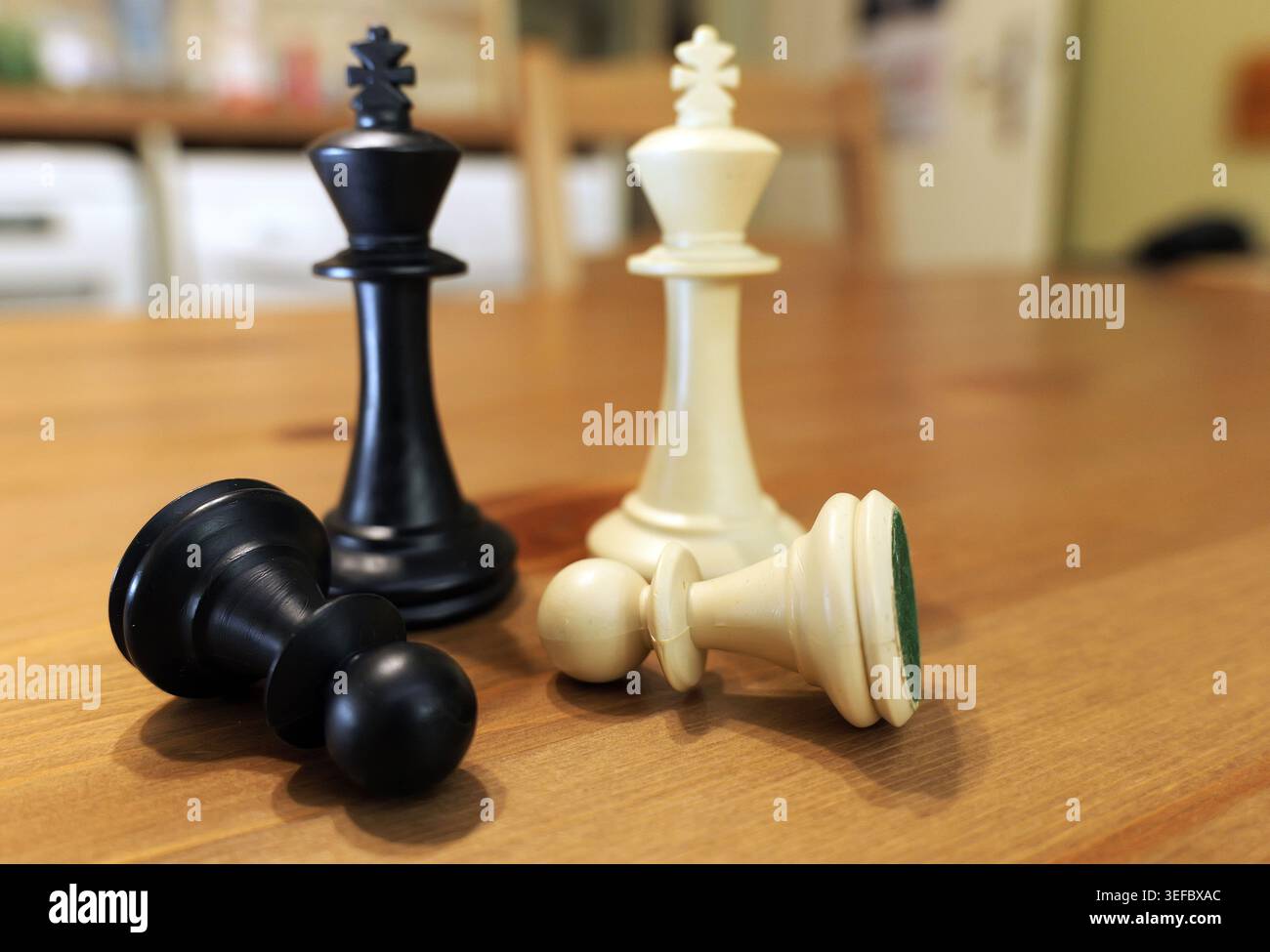 Re degli scacchi e pedine su un tavolo di legno, con due pedine cadute, simboleggiando strategia, competizione, vittoria, sconfitta, e un importante processo decisionale in b Foto Stock