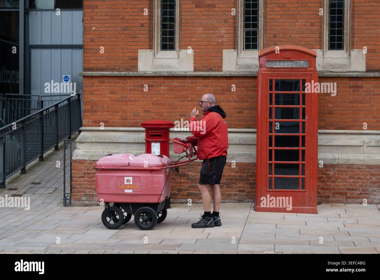 Un postino, una cassetta postale e una cassetta telefonica, Stratford-upon-Avon, Warwickshire, Regno Unito Foto Stock