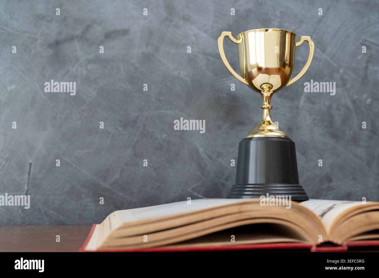 Trofeo d'oro che emerge da un libro aperto, che descrive l'eccellenza accademica, il successo dell'apprendimento, il raggiungimento degli studenti, gli obiettivi delle borse di studio, ed educativo Foto Stock