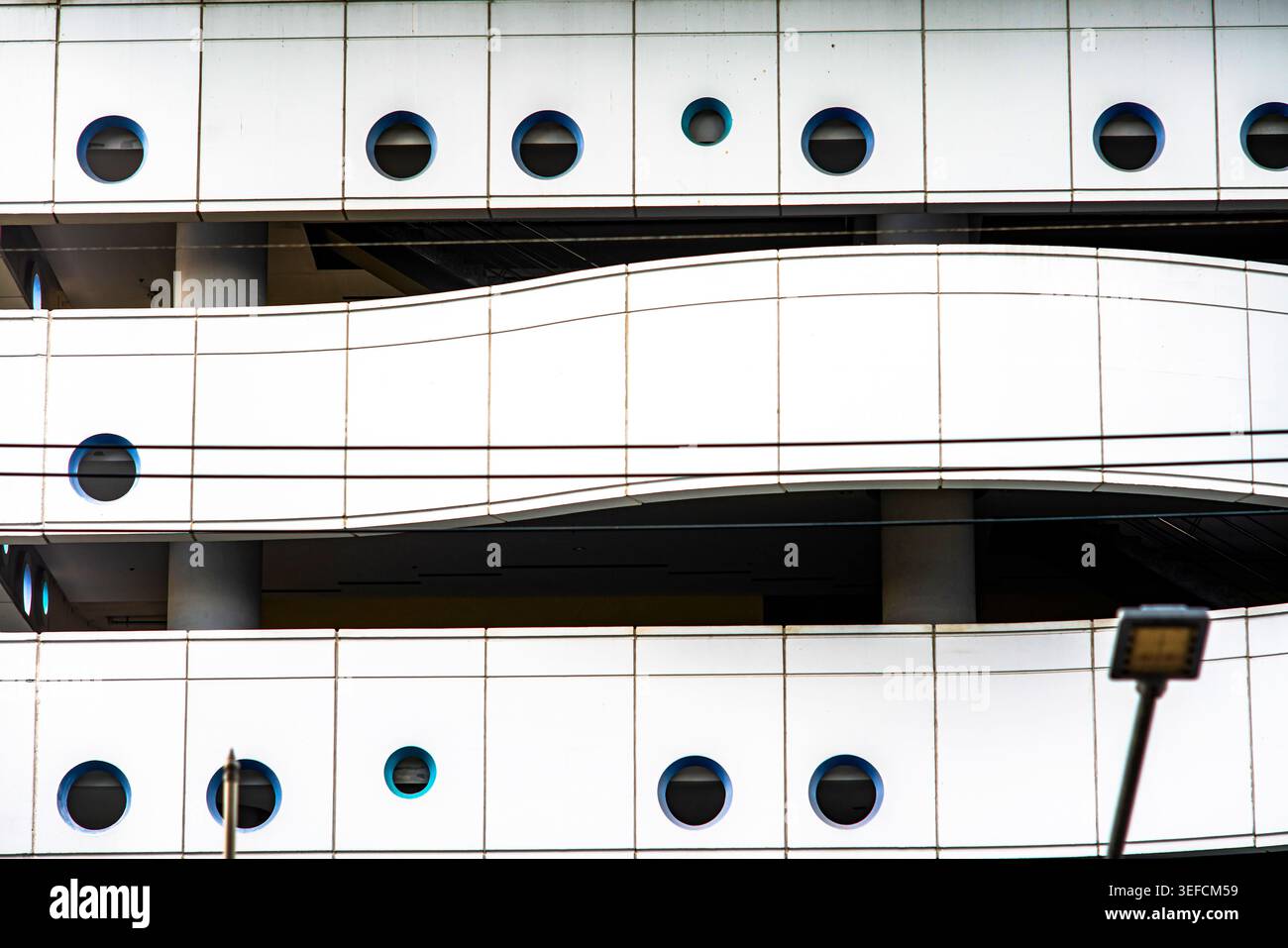 Questa immagine mostra l'esterno di un edificio moderno caratterizzato da una facciata liscia con finestre circolari e un balcone curvo, a dimostrazione di contemporaneità Foto Stock