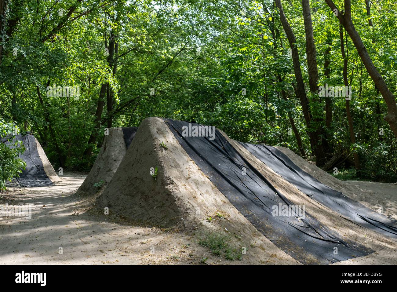 Le rampe per il salto in terra per BMX e le mountain bike sono coperte da teloni protettivi neri in un campo di pratica all'aperto in una foresta. Foto Stock