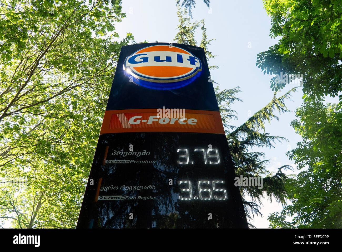 Un cartello nero alto della pompa di alimentazione mostra i prezzi della benzina G-Force, circondata da lussureggianti alberi verdi. Foto Stock