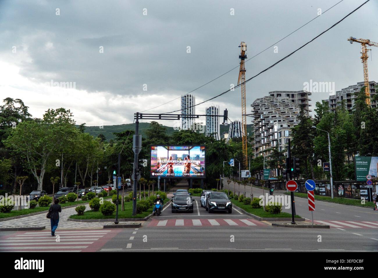 Una persona cammina attraverso un incrocio su una strada della città con auto parcheggiate nelle vicinanze. Foto Stock