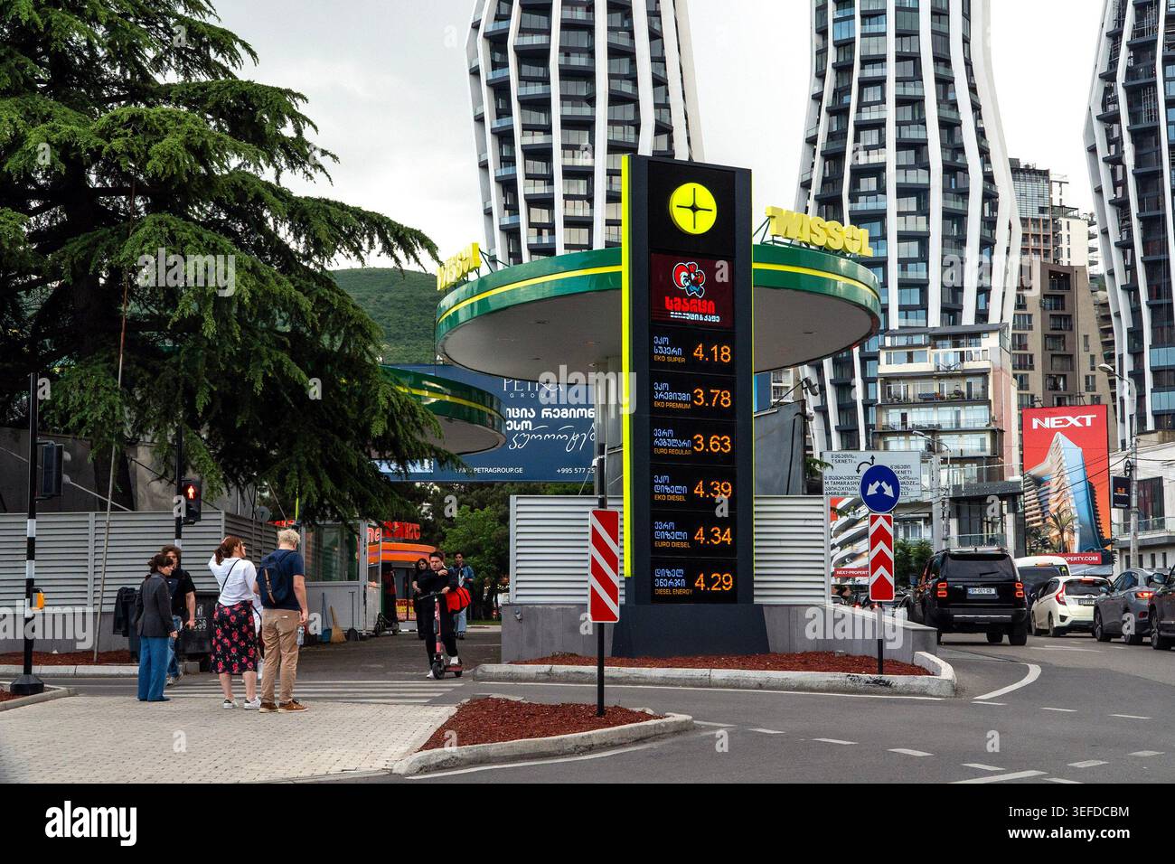 Un'insegna della stazione di servizio mostra i prezzi del carburante di fronte a edifici moderni dall'architettura curva. Foto Stock