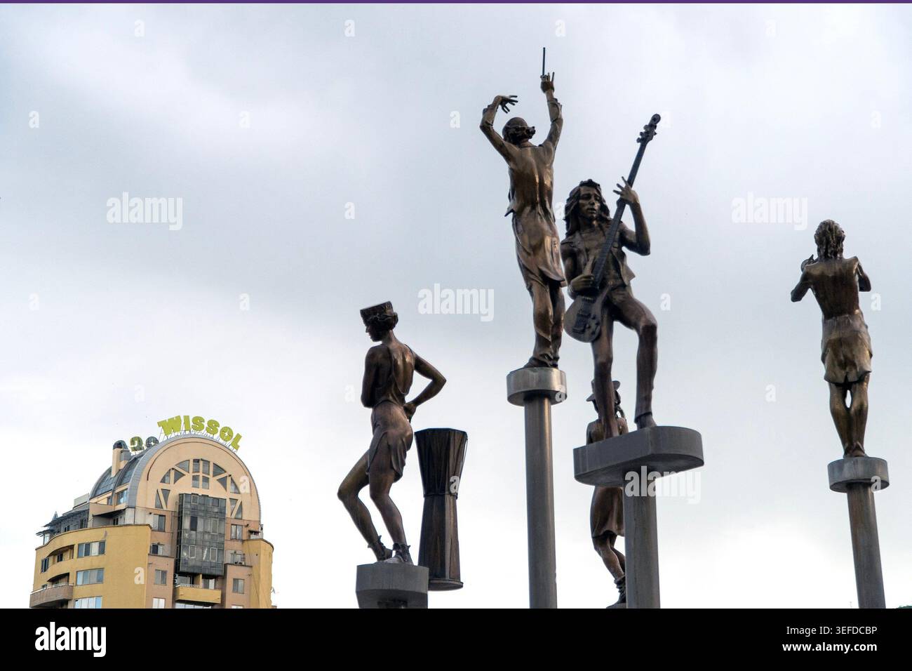 Quattro statue in bronzo si trovano di fronte ad un edificio giallo con il cartello 'Wissol' sul tetto. Foto Stock