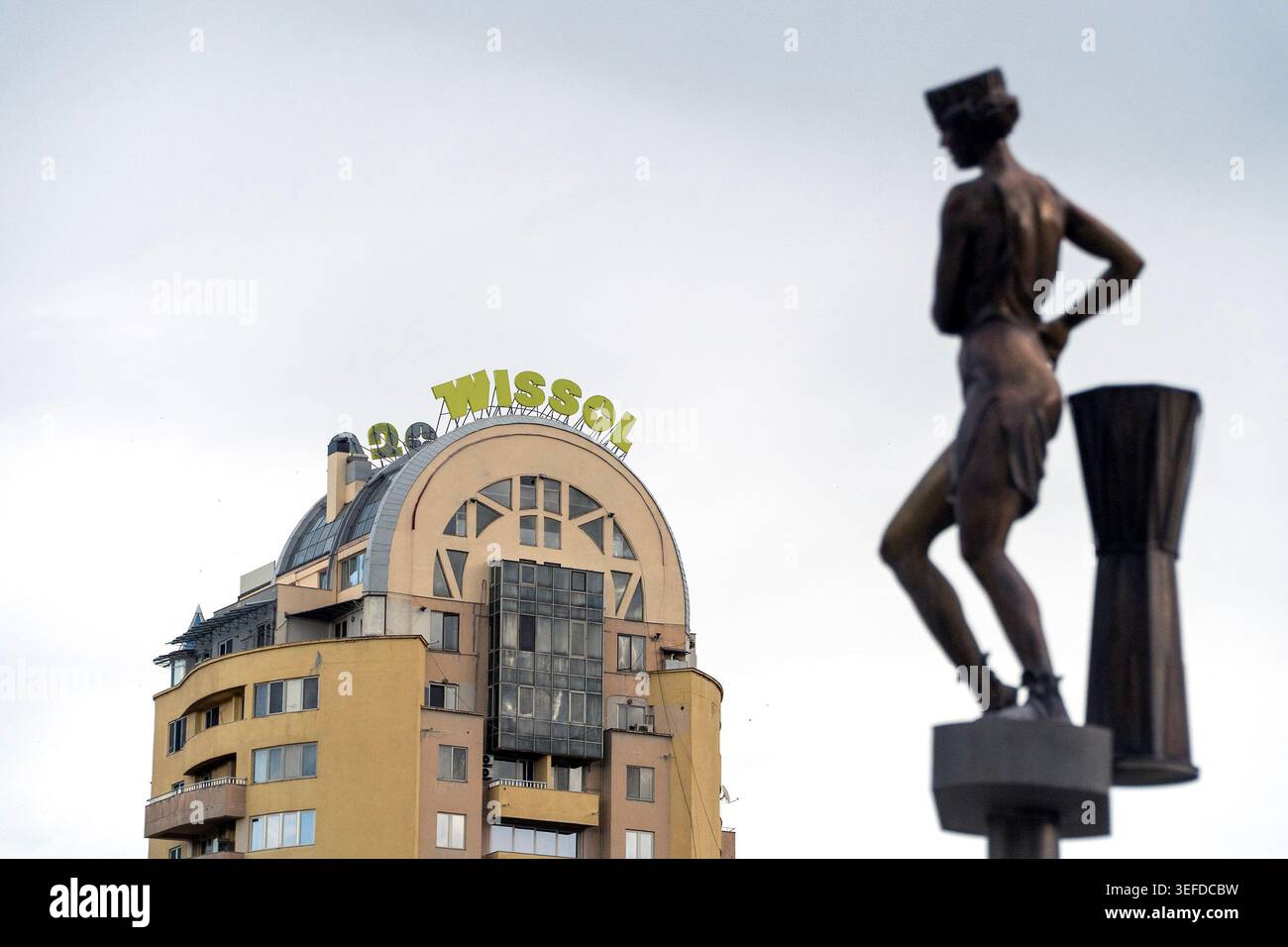 Una statua in bronzo si erge di fronte ad un edificio giallo con il cartello 'Wissol' sul tetto. Foto Stock