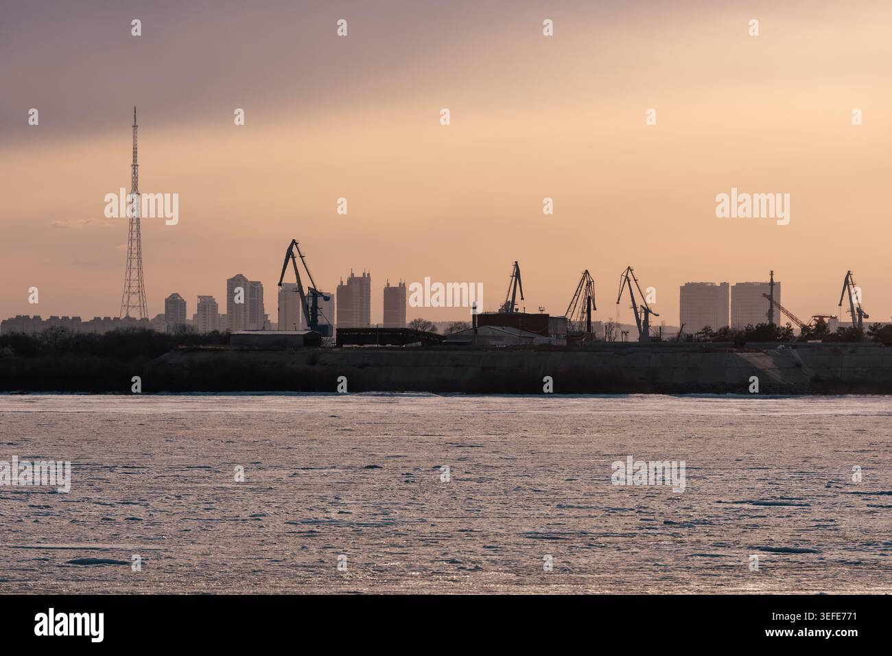 Lungomare industriale con gru e skyline della città durante il tramonto colorato. Blagoveshchensk, Russia Foto Stock