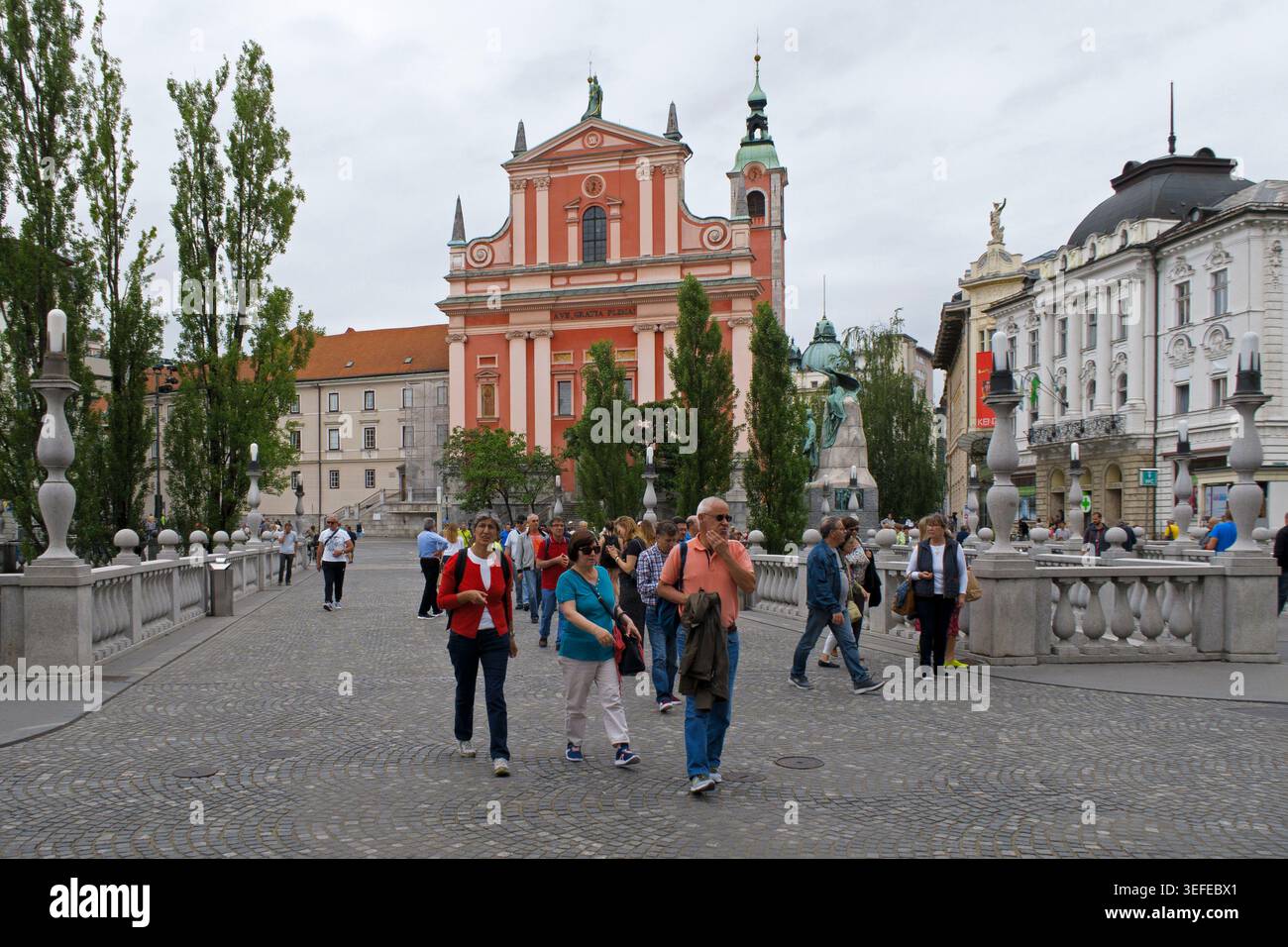 I turisti camminano attraverso lo storico Ponte triplo verso Piazza Prešeren e la Chiesa francescana dell'Annunciazione a Lubiana, Slovenia Foto Stock