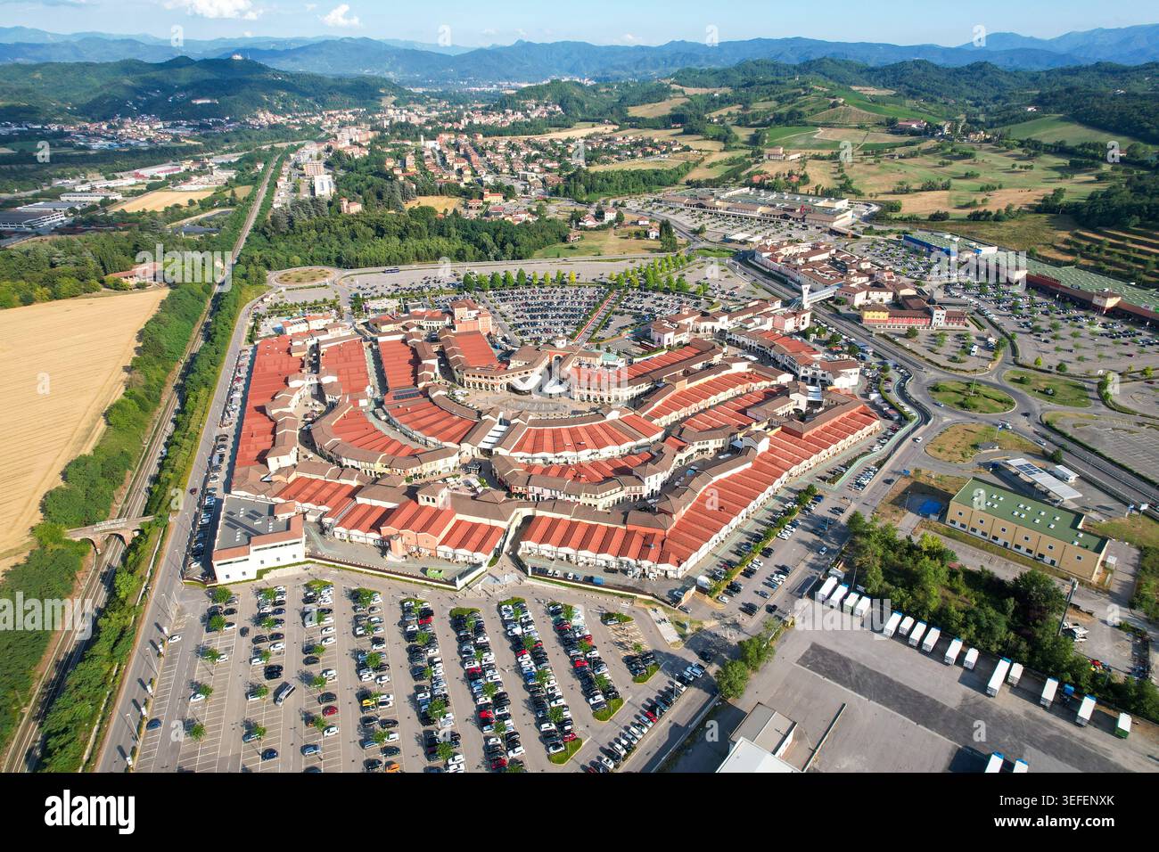 Vista aerea del Designer Outlet Serravalle con i suoi caratteristici edifici dal tetto rosso e le ampie aree di parcheggio circondate dalle dolci colline di Serrava Foto Stock