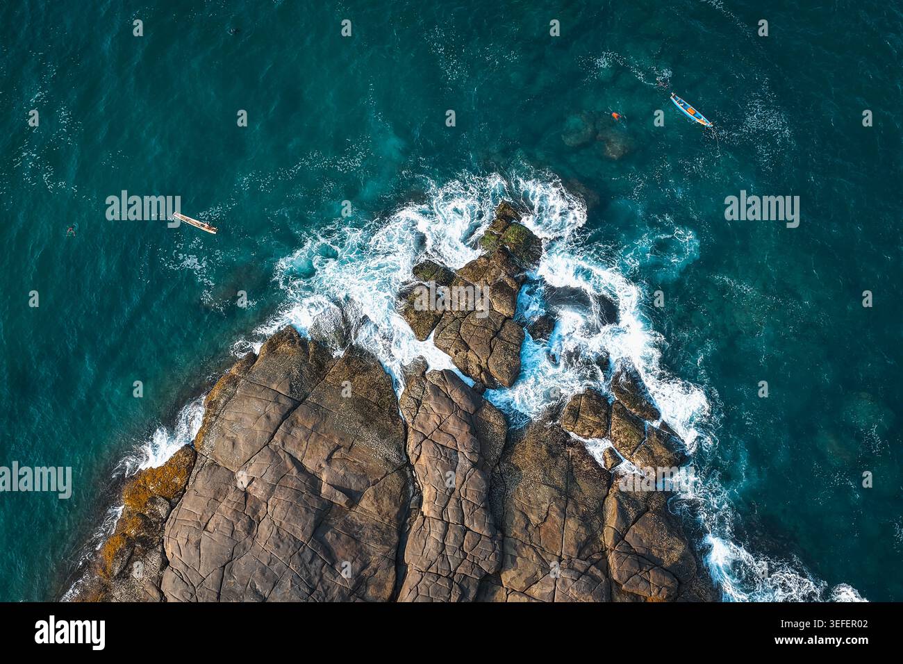 Vista aerea del promontorio roccioso con onde che si infrangono contro la riva e piccole barche da pesca nel mare turchese di Kovalam, Kerala, India. Foto Stock