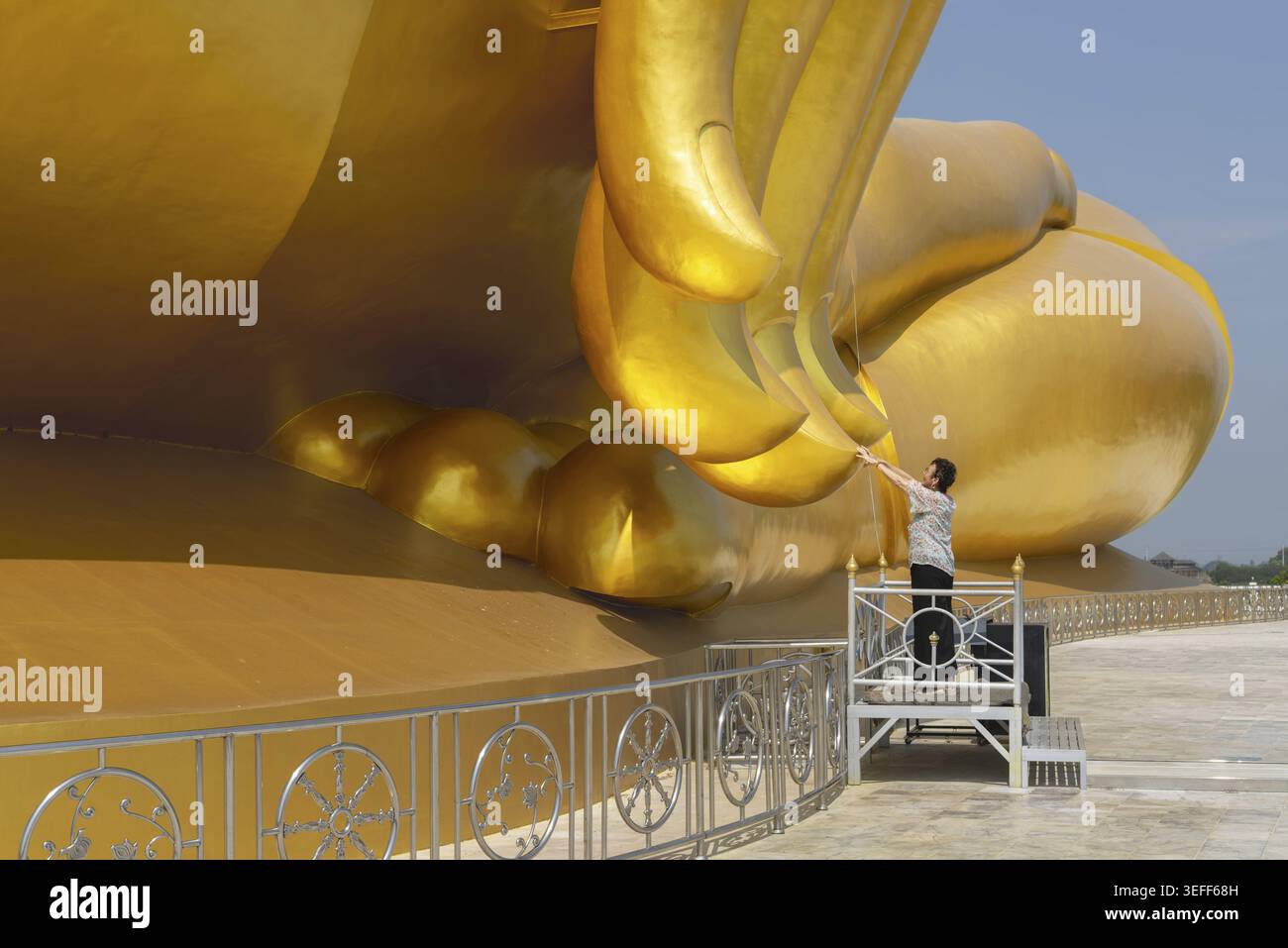 La più grande statua di Buddha in Thailandia (Luang Pho Yai), donna 60-70 tocca le dita della statua perché, secondo la credenza locale, ciò porta bene Foto Stock
