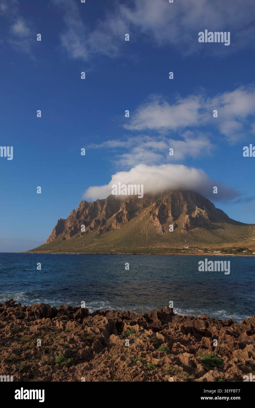 Monte cofano avvolto nel suo caratteristico berretto nuvoloso, visto da Cornino attraverso le acque cristalline della costa siciliana, Trapani. Foto Stock
