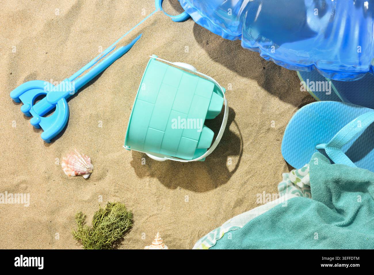 Accessori da spiaggia colorati su sabbia calda con infradito, secchio, pala, conchiglie e galleggiante gonfiabile alla luce solare estiva. Foto Stock