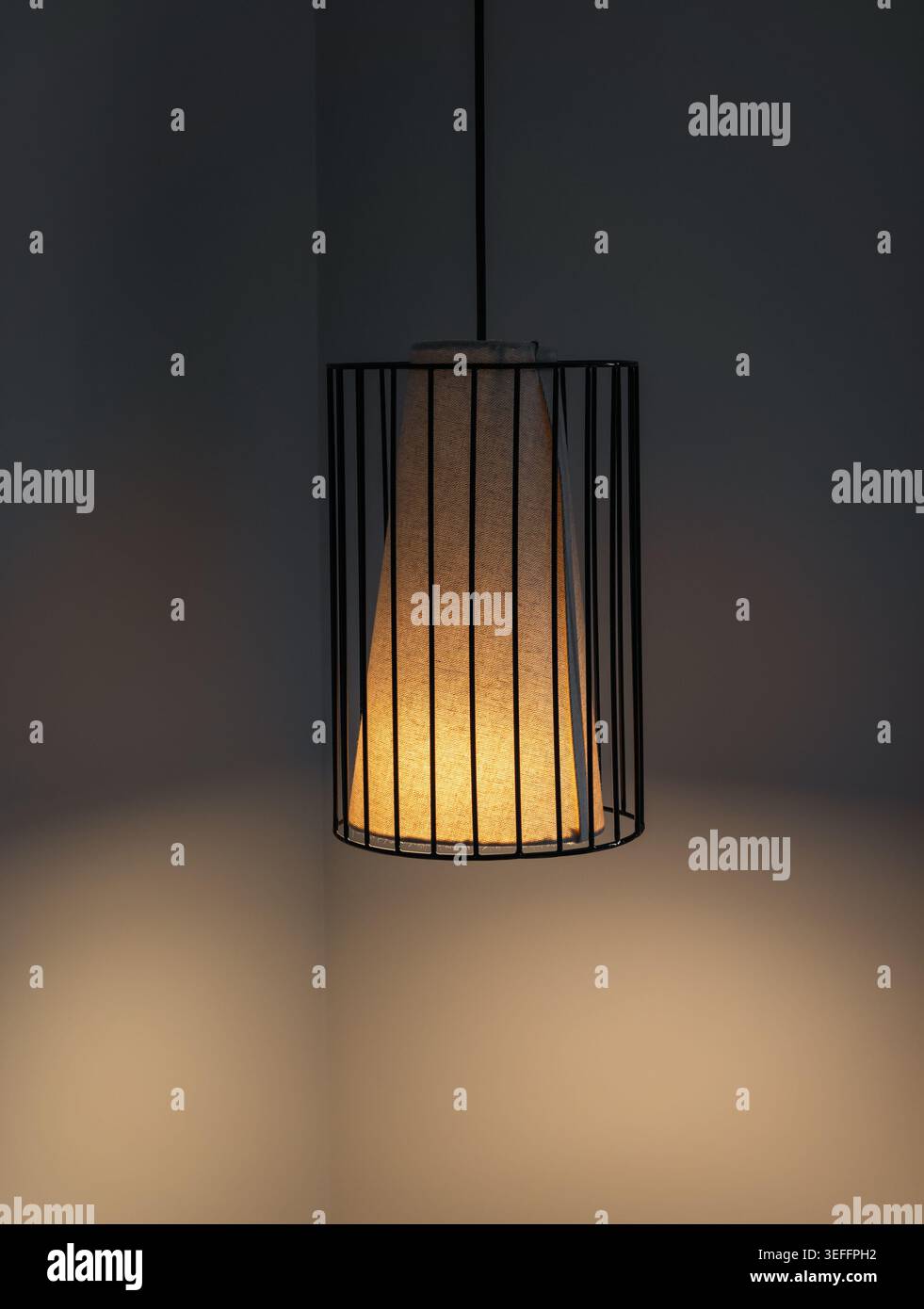Lampada a sospensione moderna con gabbia in metallo e tessuto beige. Lampada a sospensione con gabbia metallica nera in stile loft con luce calda e soffusa che illumina un angolo grigio scuro. Foto Stock