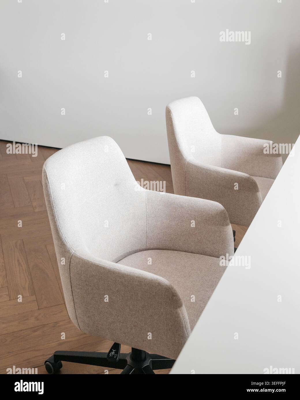 Due sedie ergonomiche imbottite beige in uno spazio di lavoro minimalista con scrivania bianca. Ripresa ad alto angolo di un paio di moderne sedie da ufficio in tessuto. Foto Stock