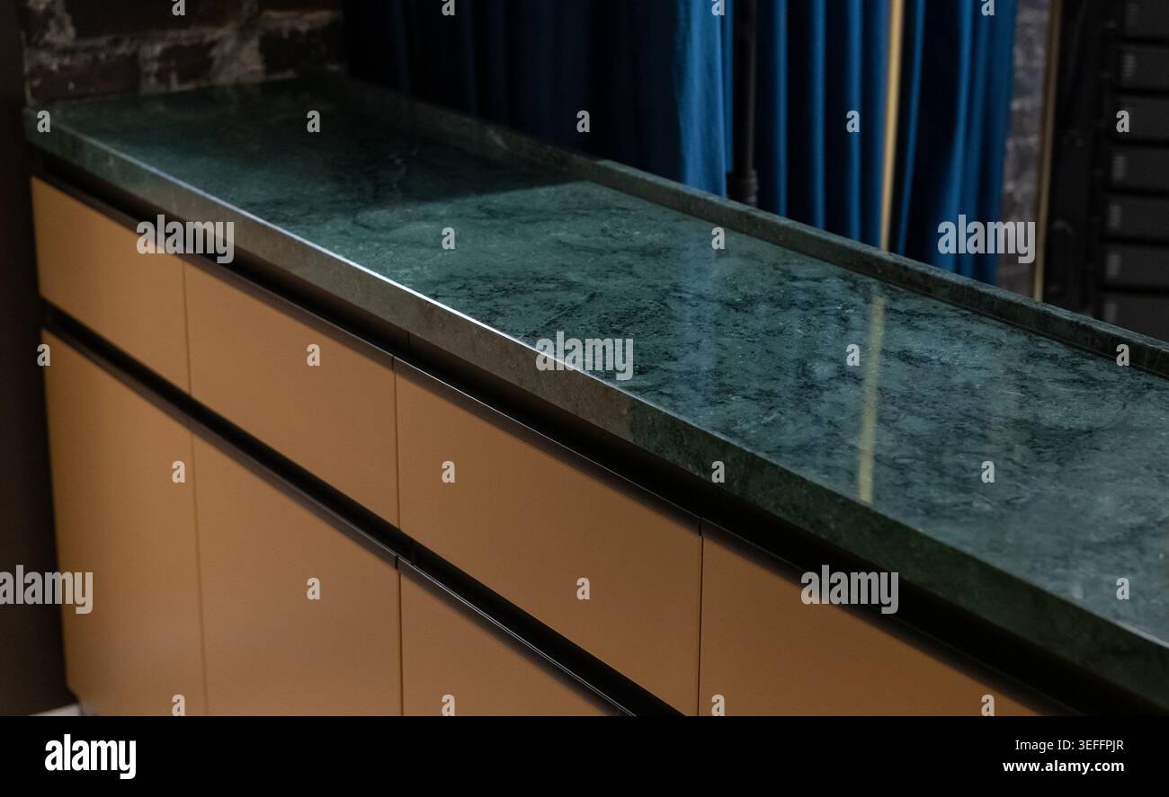 Armadio moderno con ripiano in marmo verde e cassetti opachi. Primo piano di un'isola di cucina di lusso con un ripiano in marmo verde lucido. Foto Stock
