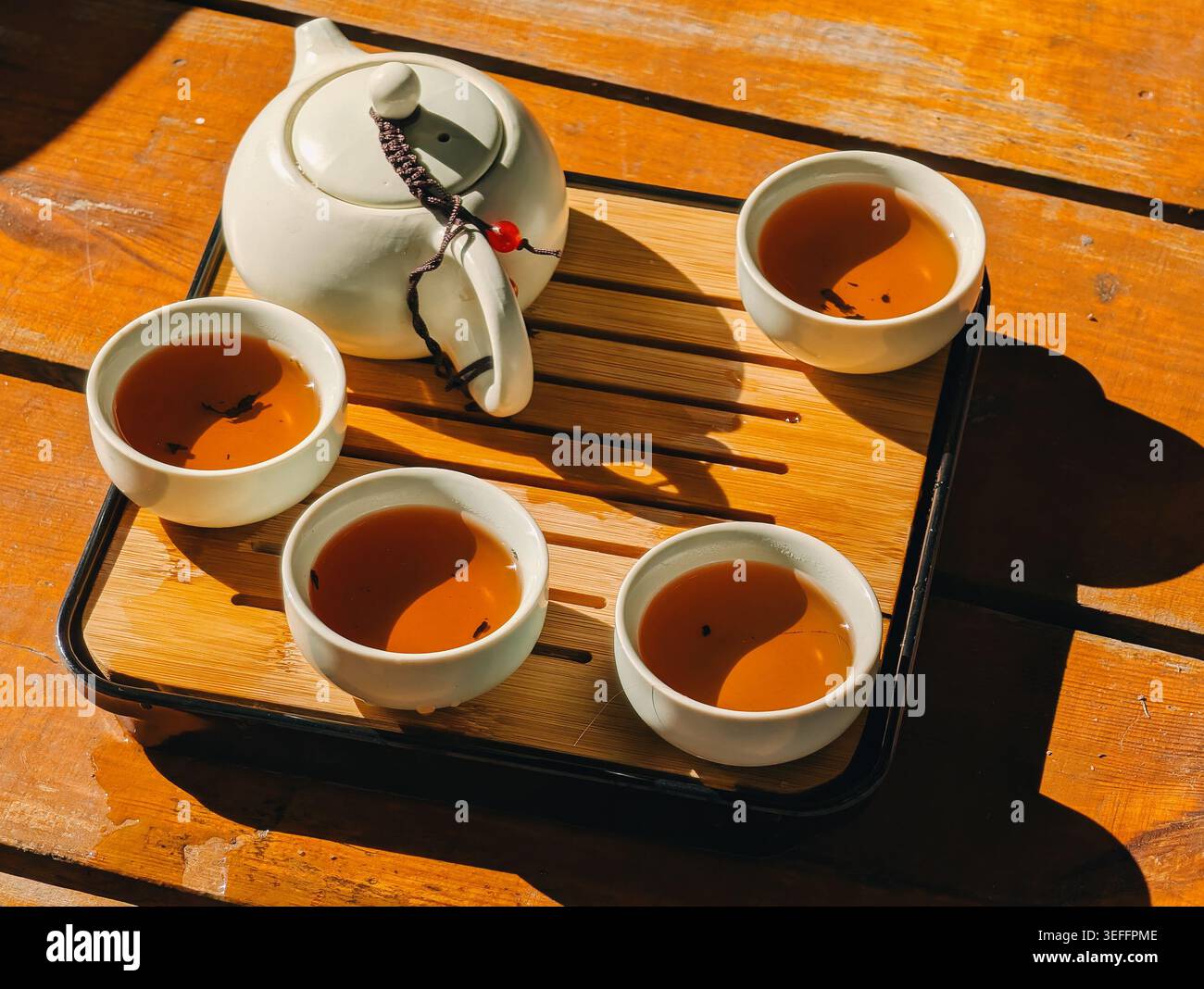 Set da tè cinese con teiera bianca e quattro tazze su vassoio di bambù Una teiera bianca in ceramica e quattro tazze riempite di tè ambrato sul vassoio di bambù Foto Stock