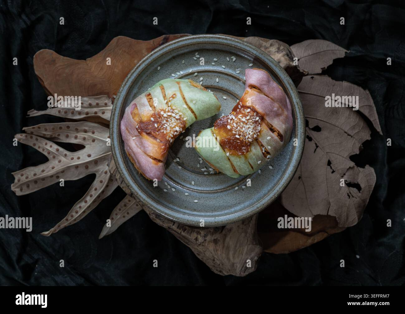 Accoccolati su un letto di foglie autunnali intemperie e accenti di legno naturale, due delicati panini a forma di mezzaluna che arrossiscono con sfumature pastello di lavanda Foto Stock