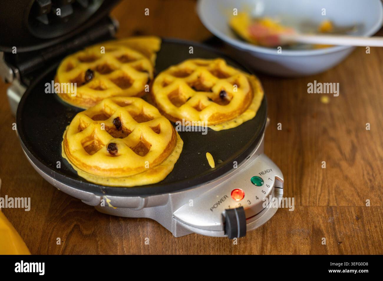 Waffle fatti in casa caldi dorati cucinati con la macchina per il ferro da stiro per una deliziosa colazione mattutina con un recipiente per impasti che ti regaleranno un'atmosfera accogliente e rilassante Foto Stock