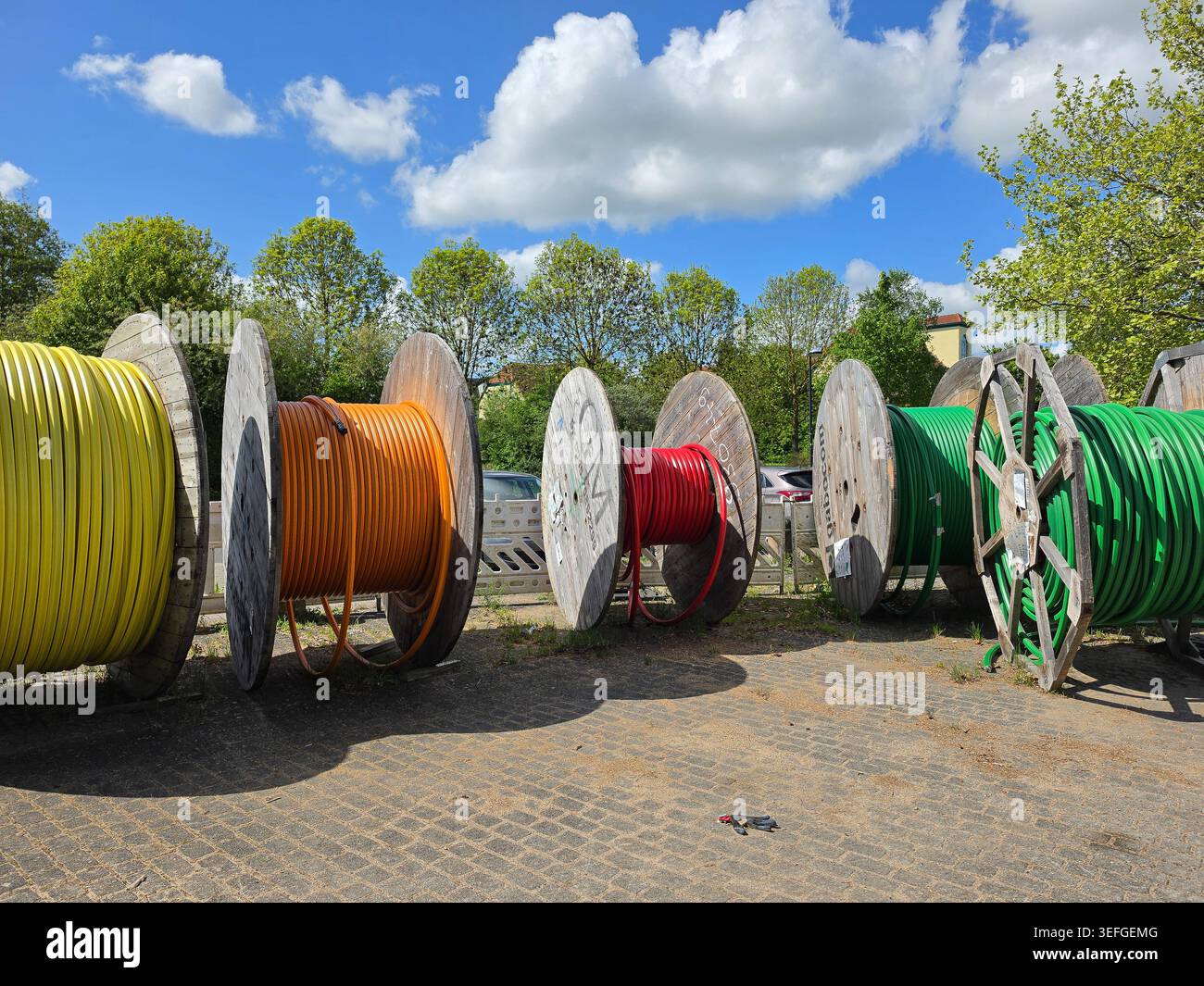 Grandi bobine di legno caricate con cavi elettrici colorati sono disposte in un'area di stoccaggio industriale all'aperto sotto un cielo blu luminoso con cl diffuso Foto Stock