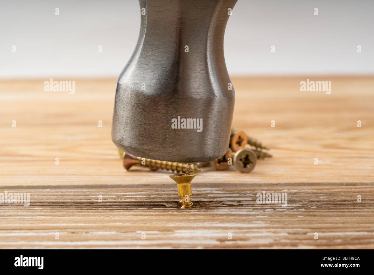Il martello colpisce la vite. Una soluzione rapida ma inefficiente. Primo piano con viti dorate, struttura macro hardware industriale Foto Stock
