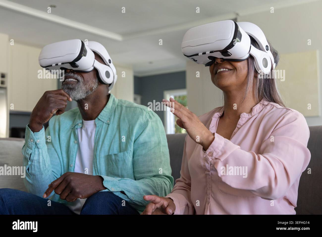 Coppia senior che indossa occhiali VR bianchi seduti sul divano in salotto per esplorare la scena virtuale Foto Stock