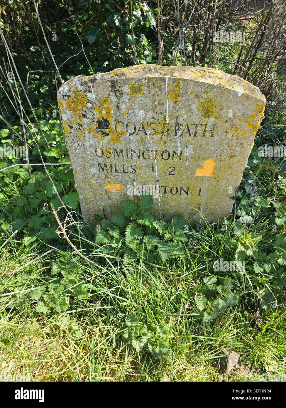 Un cartello segnaletico in pietra ricoperto di licheni per la strada costiera verso Osmington Mills, Dorset, Inghilterra, Regno Unito - Immagine stock catturata con smartphone