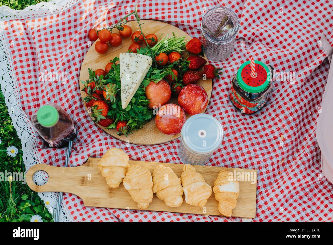 Picnic estivo con formaggio, frutta fresca e croissant su una coperta rossa Foto Stock