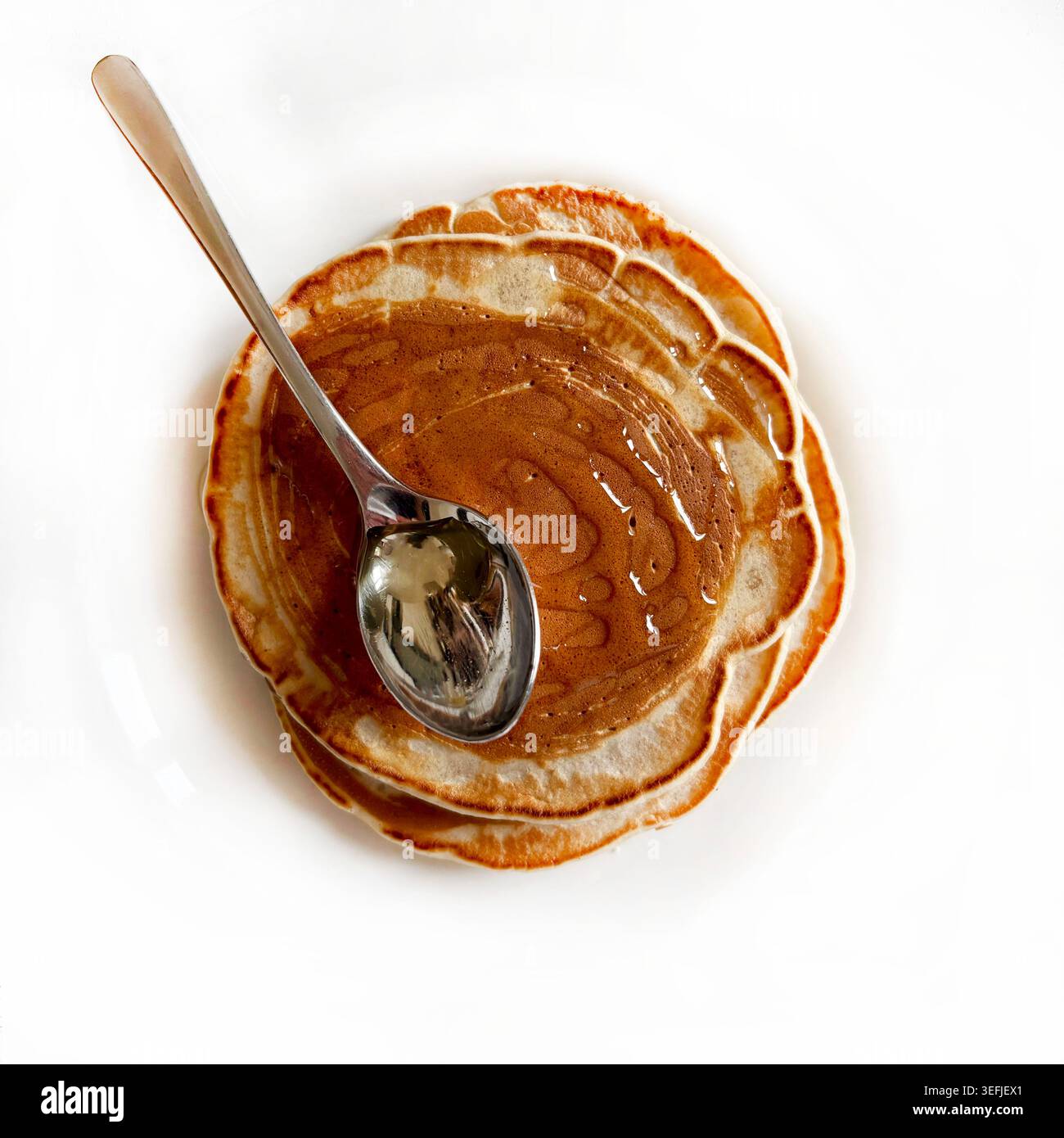 Vista dall'alto delle frittelle americane piene di sciroppo dolce e un cucchiaio d'acciaio. Gustosa colazione o brunch. Fotografia pulita e minimalista del cibo. Foto Stock