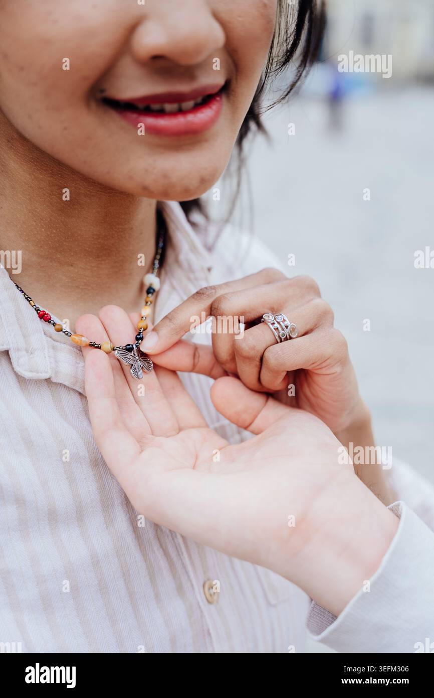 Donna asiatica che tiene in mano un ciondolo con collana a farfalla durante la romantica data della città Foto Stock