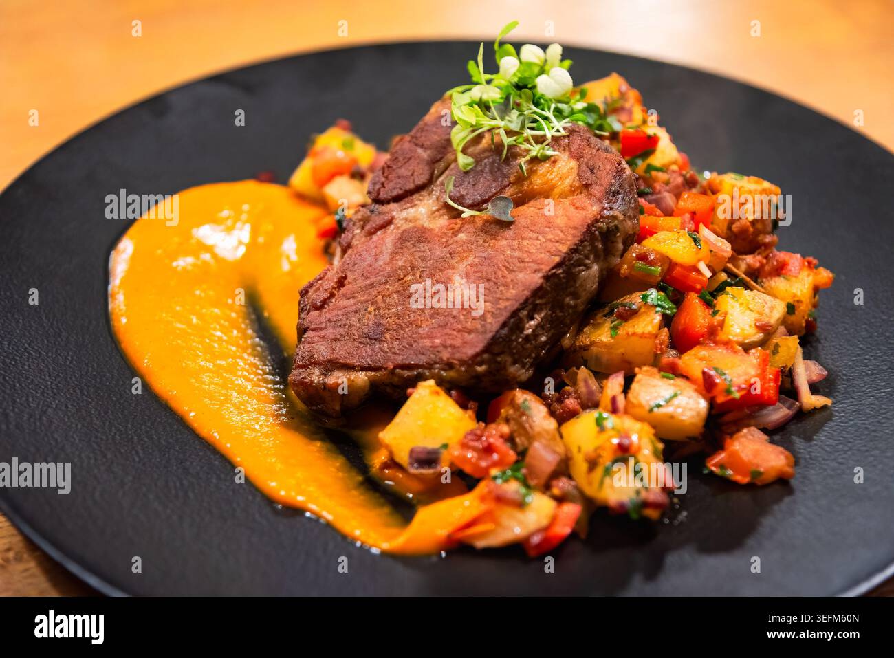 Abbondante portata principale con carne arrosto, patate colorate e purea di arancia luminosa servita su un elegante piatto scuro Foto Stock