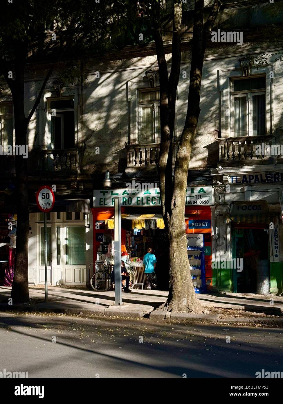 Un piccolo negozio di quartiere in Avenida Álvaro Obregón a Roma Norte, città del Messico, visto attraverso le spettacolari ombre degli alberi e la luce del tardo pomeriggio - Immagine stock catturata con smartphone