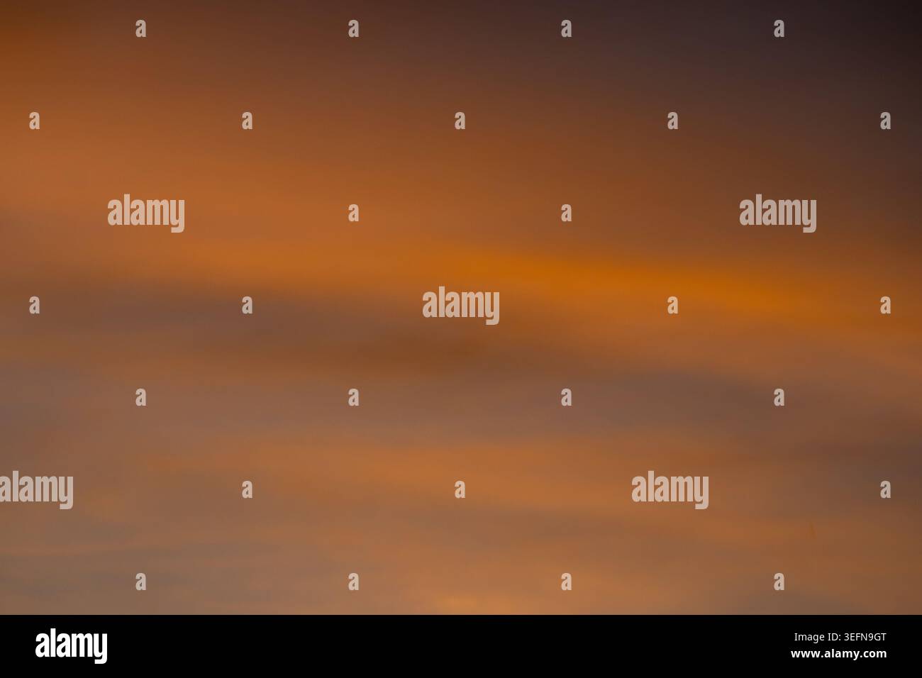 Cielo morbido sfocato con tonalità calde di arancio e ambra che si fondono con bande nuvolose a strati in una sfumatura astratta Foto Stock